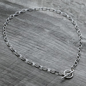 Puede incluir: Un collar de cadena de plata con cierre de palanca. La cadena está hecha de eslabones ovalados.