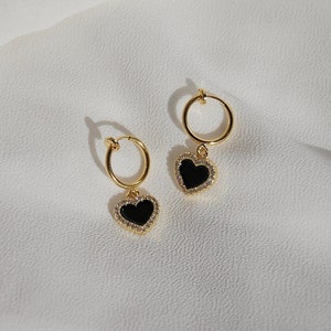 A single small 18-karat-gold plated and clear cubic zirconia crystal bordered black acrylic resin heart-shaped charm dangling from a small thin 18-karat-gold plated clip-on huggie hoop closure, which is hypoallergenic, nickel-free, and invisible.