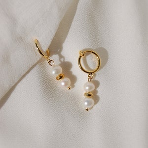 Two small-sized cream white round natural freshwater pearls with an 18 karat gold plated round spacer in-between dangling from a small thin 18-karat-gold plated clip-on huggie hoop closure, which is hypoallergenic, nickel-free, and invisible.