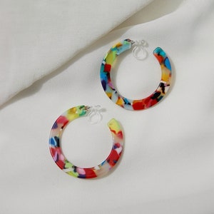 Large thin flat circular acrylic resin modern geometric-style tortoise shell hoops (colors: red, orange, pink, yellow, blue, green, purple, black, and white) secured by hypoallergenic and nickel-free acrylic invisible clip-on earring closures.