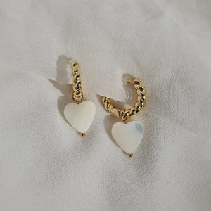 Medium-sized cream white heart-shaped natural freshwater pearl shells dangling from small 18-karat-gold plated twisted huggie hoops secured by hypoallergenic and nickel-free acrylic invisible clip-on closures.