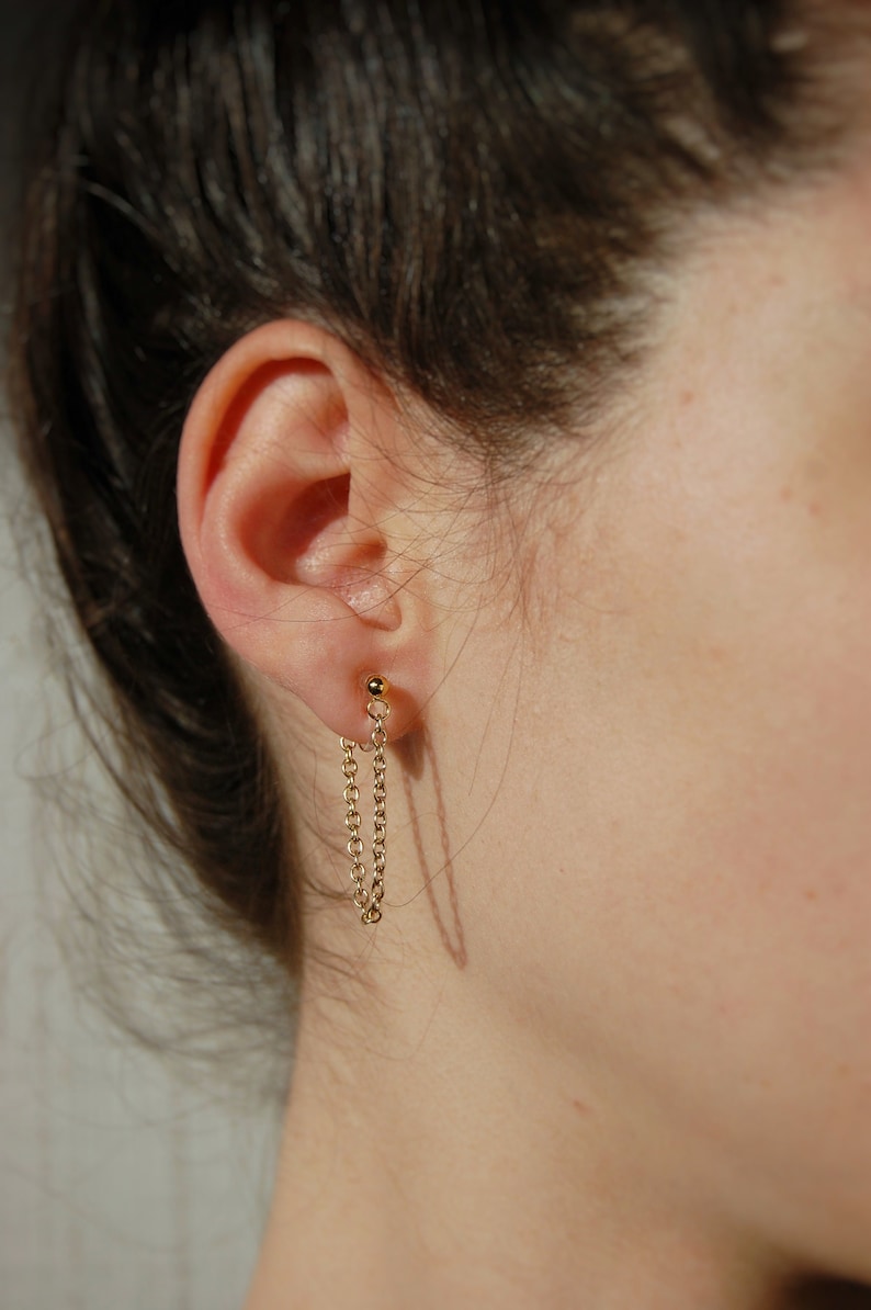 A medium-length loop of thin 18 karat gold plated chain wraped from the front to the back of the ear in the form of a threader earring, secured by 18 karat gold clip-on ball posts which are hypoallergenic, nickel-free, and clear invisible acrylic.