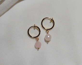 May include: A pair of gold hoop earrings with a pink stone charm hanging from each hoop.