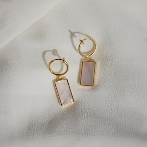 May include: A pair of gold hoop earrings with a rectangular white mother-of-pearl charm hanging from each hoop.