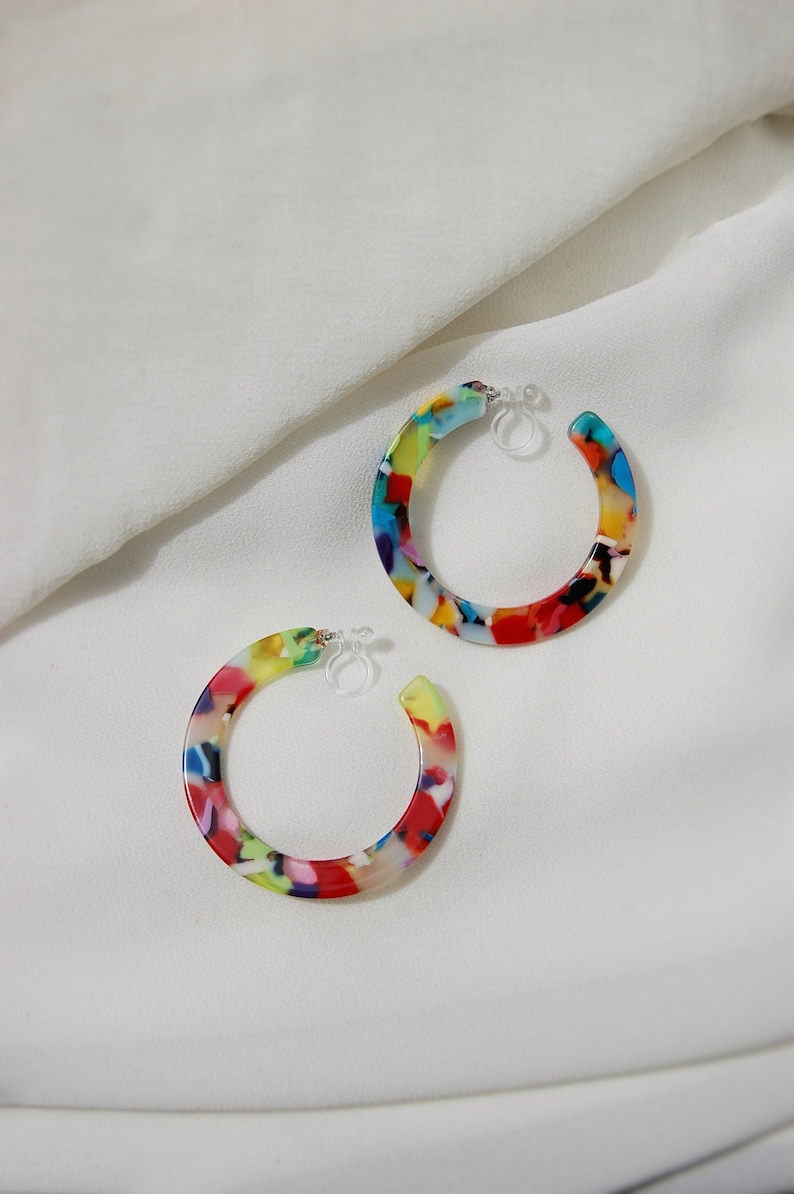 Large thin flat circular acrylic resin modern geometric-style tortoise shell hoops (colors: red, orange, pink, yellow, blue, green, purple, black, and white) secured by hypoallergenic and nickel-free acrylic invisible clip-on earring closures.