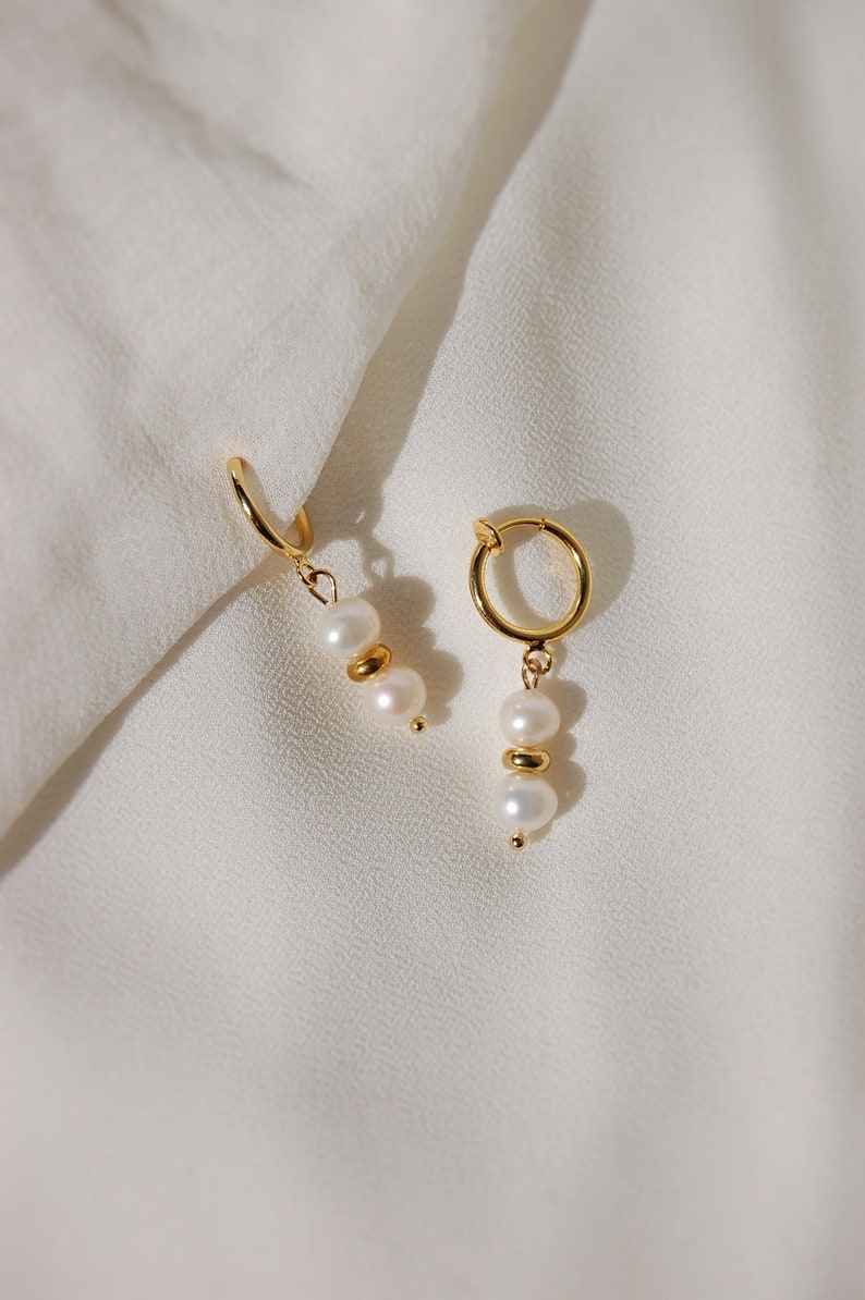 Two small-sized cream white round natural freshwater pearls with an 18 karat gold plated round spacer in-between dangling from a small thin 18-karat-gold plated clip-on huggie hoop closure, which is hypoallergenic, nickel-free, and invisible.