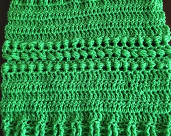 Pode incluir: Um quadrado de crochê verde com um padrão texturizado. O quadrado tem um design em relevo no centro e uma borda canelada.