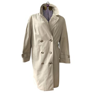 May include: A beige double-breasted trench coat with a wide collar and buttoned cuffs. The coat has a classic design with a belted waist and a long length, suitable for outerwear.