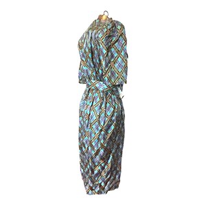 K&ouml;nnte beinhalten: Ein blaues und goldenes kariertes Kleid mit einem selbstgebundenen G&uuml;rtel. Das Kleid hat kurze &Auml;rmel und eine figurbetonte Silhouette.