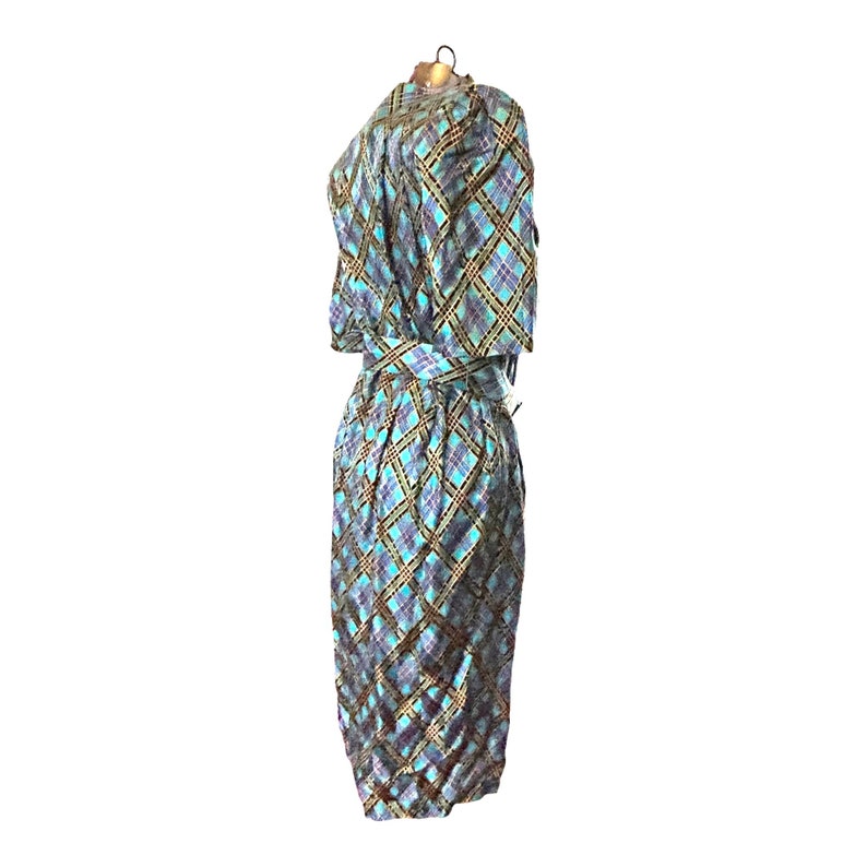 K&ouml;nnte beinhalten: Ein blaues und goldenes kariertes Kleid mit einem selbstgebundenen G&uuml;rtel. Das Kleid hat kurze &Auml;rmel und eine figurbetonte Silhouette.