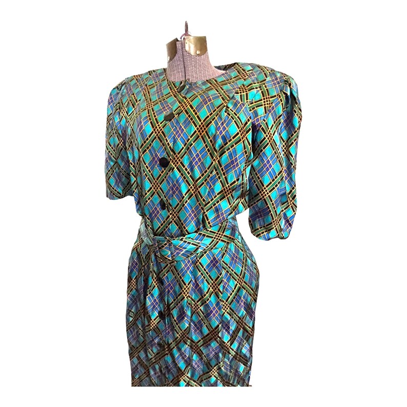 K&ouml;nnte beinhalten: Ein blaues und gr&uuml;nes kariertes Kleid mit G&uuml;rtel und kurzen &Auml;rmeln. Das Kleid hat einen Knopfleisten vorne und einen runden Ausschnitt.