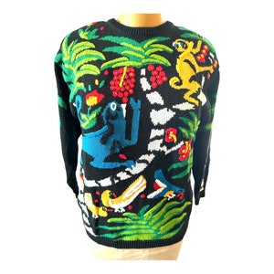 Può includere: Maglione nero a maglia con una colorata scena della giungla. Il maglione presenta una rana blu, una scimmia gialla e vari uccelli e fiori. Nel design è presente anche un fogliame verde e giallo.