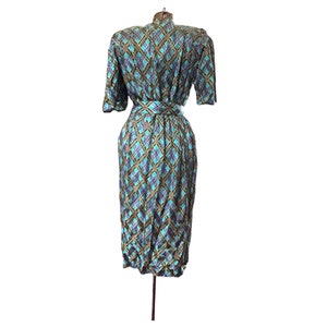 K&ouml;nnte beinhalten: Ein blaues und goldenes kariertes Kleid mit kurzen &Auml;rmeln und einem G&uuml;rtel. Das Kleid ist auf einer Puppe.