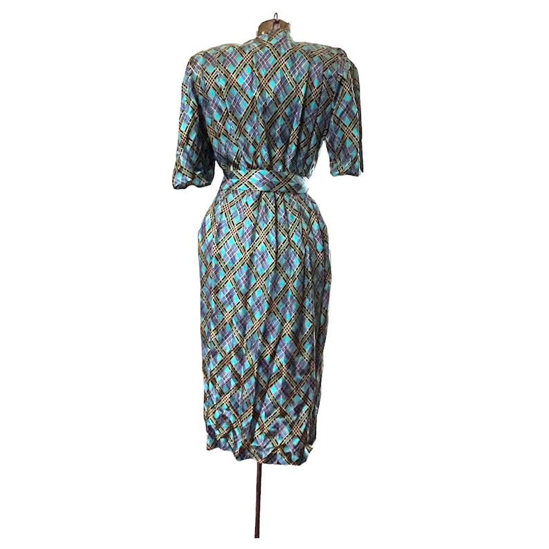 K&ouml;nnte beinhalten: Ein blaues und goldenes kariertes Kleid mit kurzen &Auml;rmeln und einem G&uuml;rtel. Das Kleid ist auf einer Puppe.
