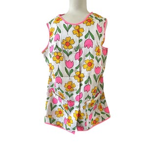 May include: A sleeveless, white floral print top with yellow and pink flowers, green leaves, and a pink trim. The top has a button-up front and two pockets. The fabric has vertical stripes.