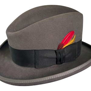 Pode incluir: Um chapéu fedora cinza com uma fita preta e um detalhe de pena vermelha e amarela.
