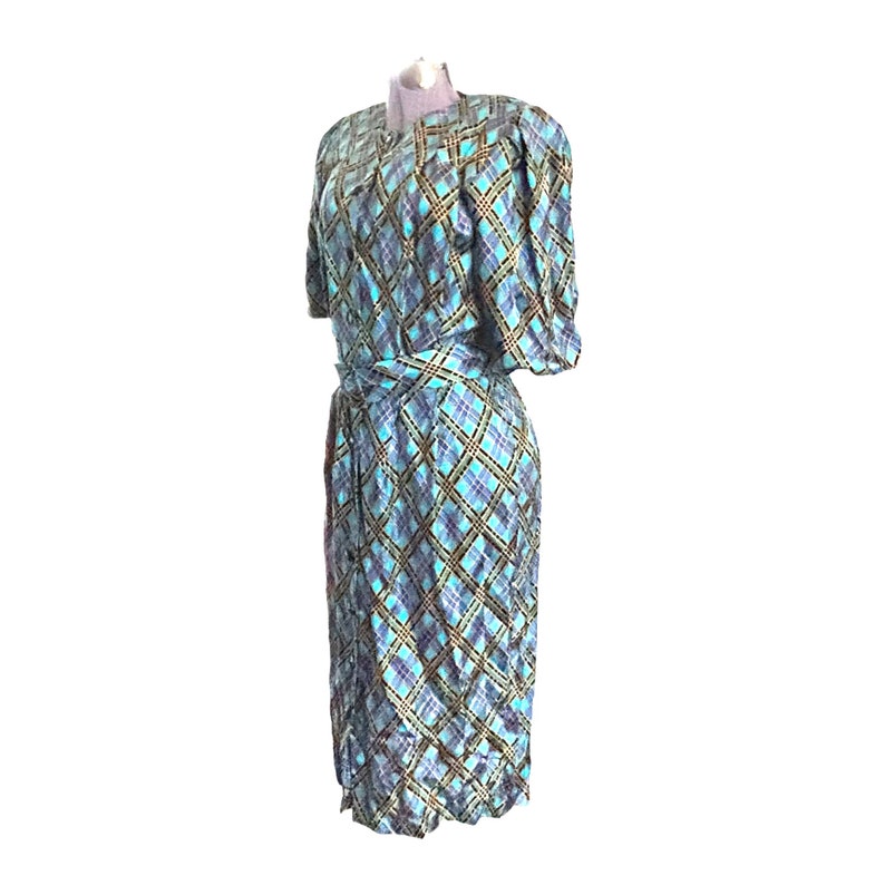 K&ouml;nnte beinhalten: Ein blaues und braunes kariertes Kleid mit einem selbstgebundenen G&uuml;rtel. Das Kleid hat kurze &Auml;rmel und einen knielangen Rock.