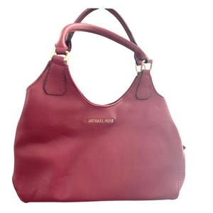 May include: A burgundy leather handbag with gold hardware and the Michael Kors logo.