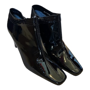 May include: A pair of black patent leather ankle boots with a square toe and stiletto heel. The boots have a glossy finish and a zipper closure. The heel height appears to be approximately 3 inches.