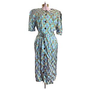K&ouml;nnte beinhalten: Ein blaues und gr&uuml;nes kariertes Kleid mit Knopfleiste und G&uuml;rtel. Das Kleid hat kurze &Auml;rmel und einen knielangen Rock.