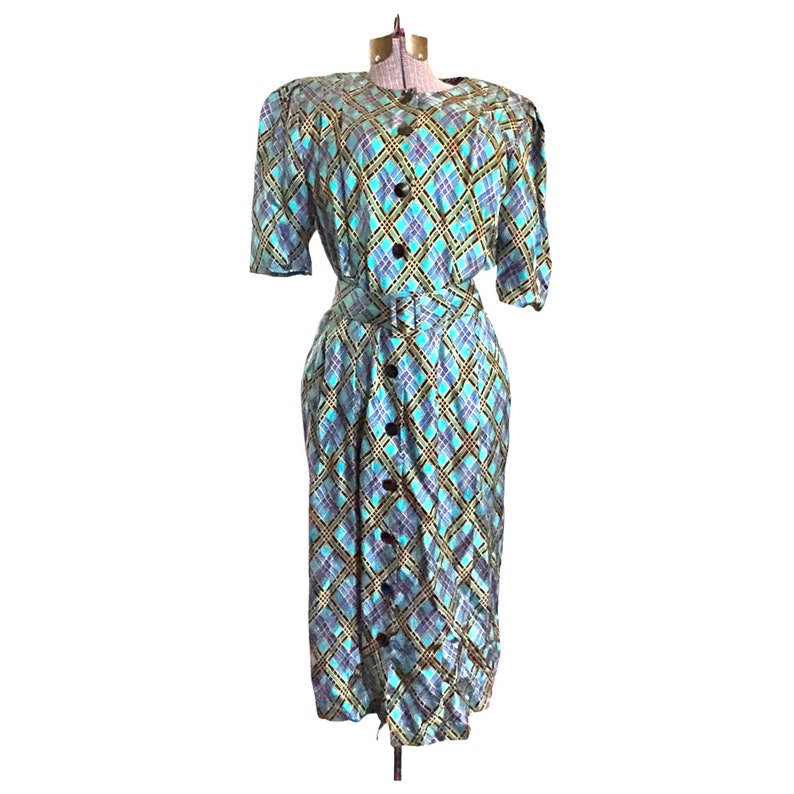 K&ouml;nnte beinhalten: Ein blaues und gr&uuml;nes kariertes Kleid mit Knopfleiste und G&uuml;rtel. Das Kleid hat kurze &Auml;rmel und einen knielangen Rock.