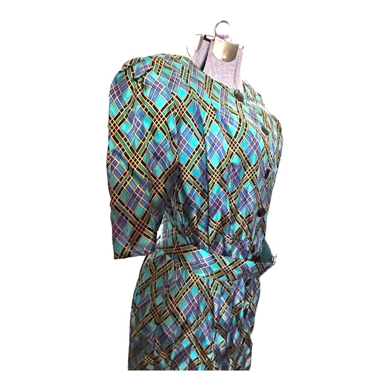 K&ouml;nnte beinhalten: Ein blaues und gr&uuml;nes kariertes Kleid mit einem schwarzen G&uuml;rtel und Kn&ouml;pfen. Das Kleid hat kurze &Auml;rmel und eine figurbetonte Silhouette.