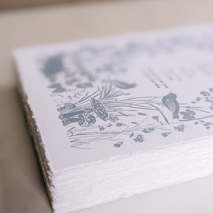 Puede incluir: Una pila de papel blanco con una ilustraci&oacute;n en tinta azul de hongos, flores y un p&aacute;jaro. El papel tiene una superficie rugosa y texturizada.