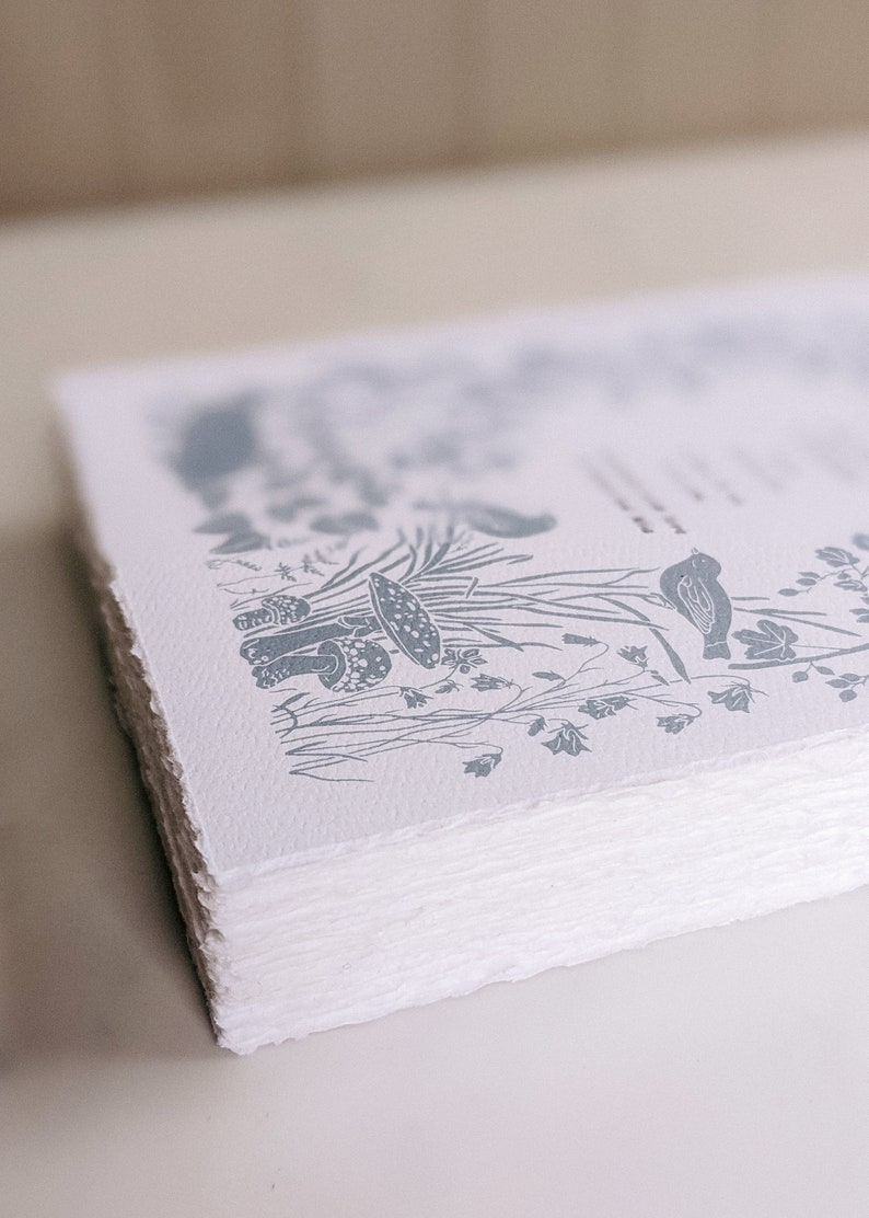 Puede incluir: Una pila de papel blanco con una ilustraci&oacute;n en tinta azul de hongos, flores y un p&aacute;jaro. El papel tiene una superficie rugosa y texturizada.