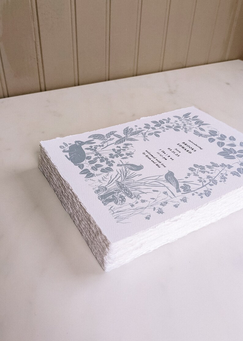 Puede incluir: Una pila de tarjetas de papel blanco con un dise&ntilde;o floral azul y el texto "Brooks Edward naci&oacute; el 03.31.23 7 lbs 8 oz bienvenido con amor por Brian y Julie"