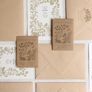 K&ouml;nnte beinhalten: Eine Sammlung von Babykarten und Wildblumensamen-P&auml;ckchen. Die Karten zeigen botanische Illustrationen und Text, einschlie&szlig;lich Babynamen und Geburtsdaten. Die Umschl&auml;ge sind hellbraun und haben ein passendes Design.
