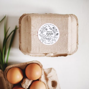Op de afbeelding: Een kartonnen eierdoos met een sticker waarop "Fresh Eggs" staat met een tekening van een kip en bloemen. De doos is gevuld met bruine eieren.