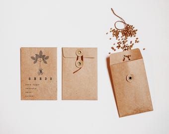 May include: Three brown paper seed packets with a plant illustration and the word "SEEDS" printed on one. One packet is open with seeds spilling out. The packets have a rustic, natural aesthetic.