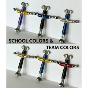 May include: Six small crosses made from horseshoes, each with a different colour wire wrapped around the horseshoe. The crosses are arranged in two rows of three. The text "SCHOOL COLORS & TEAM COLORS" is printed below the crosses.