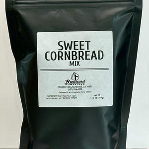 May include: A black resealable bag with a white label that reads "SWEET CORNBREAD MIX" and includes the company name "Broussard Homestead" and contact information. The bag contains 14.3 ounces (405 grams) of cornbread mix.