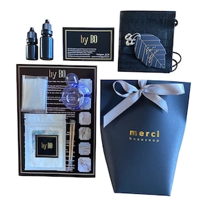 May include: An assortment of jewelry-making supplies and packaging. Includes two black bottles, a black card with gold text, a black bag with a leaf charm, a blue ring, a black box with a silver bow, and a card with the text "by BO".