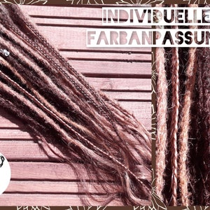 May include: A close-up of brown and blonde synthetic dreadlocks with the text "INDIVIDUELLE FARBANPASSUNG" on a wooden background.