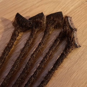 May include: Five brown hair extensions with clips attached to the ends. The extensions are arranged in a fan shape.