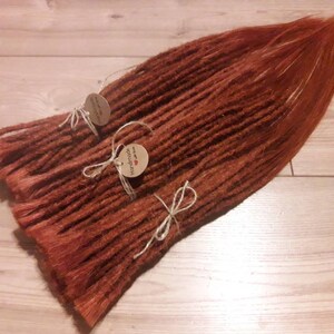 May include: A bundle of long, reddish-brown synthetic dreadlocks with brown string ties and two small brown paper tags that say "Handmade with love".