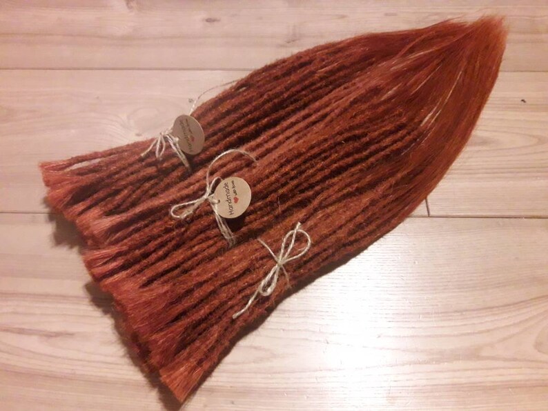 May include: A bundle of long, reddish-brown synthetic dreadlocks with brown string ties and two small brown paper tags that say "Handmade with love".