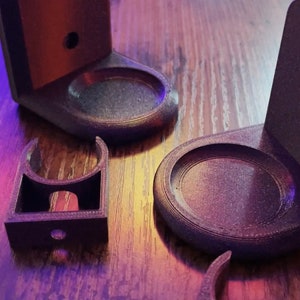 Könnte beinhalten: Zwei schwarze Wandhalter aus Kunststoff mit runden Sockeln. Die Halter sind so konzipiert, dass sie Gegenstände wie eine Zahnbürste oder einen Rasierer halten.