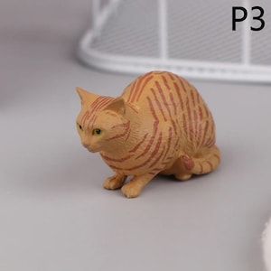 May include: A small, orange cat figurine with dark red stripes. The cat is in a crouching position, with its head lowered and eyes focused forward. The figurine has green eyes and is labeled "P3" in the upper right corner.
