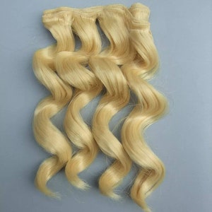 May include: Blonde human hair extensions in a wavy texture. The hair is bundled together with a weft.