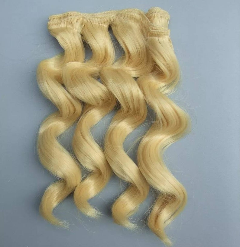 May include: Blonde human hair extensions in a wavy texture. The hair is bundled together with a weft.