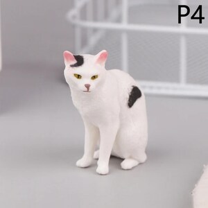 May include: A white cat figurine with black spots and pink-tipped ears. The cat has yellow eyes and is sitting upright. The figurine is a decorative item, possibly for a shelf or display.