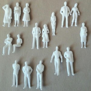 May include: A collection of small, white plastic figurines depicting various human figures in different poses. The figurines include standing, sitting, and walking figures, suitable for architectural models or miniature scenes.