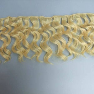 May include: A bundle of wavy blonde human hair extensions. The hair is light blonde and has a natural wave pattern.