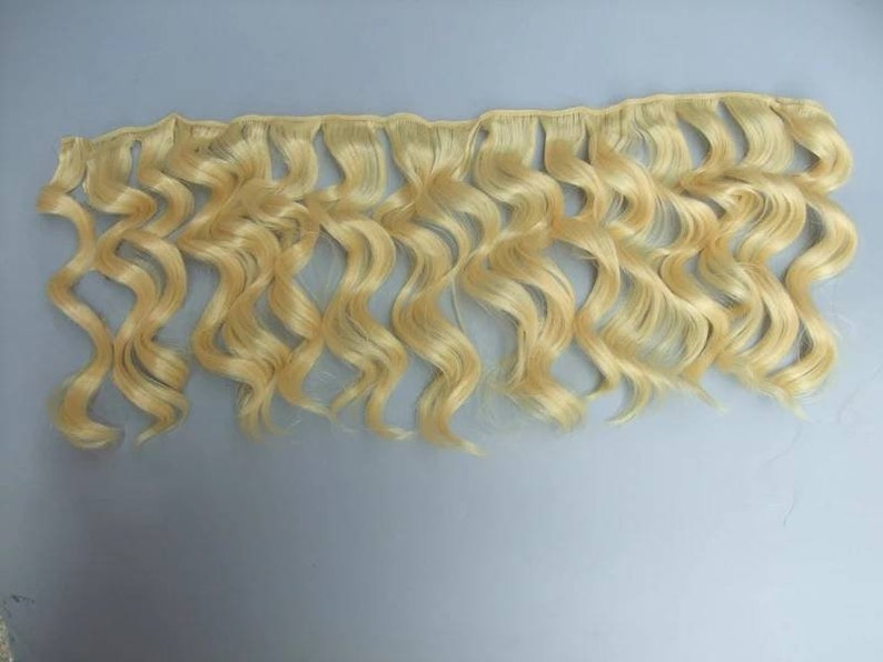 May include: A bundle of wavy blonde human hair extensions. The hair is light blonde and has a natural wave pattern.