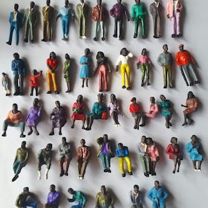 May include: A collection of miniature plastic figures of people in various poses and clothing. The figures are standing and sitting, and some are holding objects. The figures are all black and are painted in a variety of colors.
