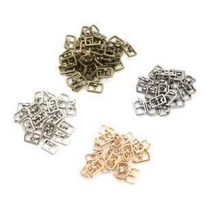 Puede incluir: Un montón de hebillas metálicas en tres colores diferentes: dorado, plateado y bronce. Las hebillas son todas del mismo tamaño y forma, y están dispuestas en un patrón aleatorio.