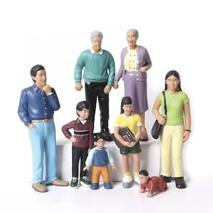 Op de afbeelding: Een verzameling miniatuurbeeldjes die een gezin van acht personen uitbeelden. De figuren omvatten een man in een blauw overhemd en lichtblauwe broek, een vrouw in een paars pak en kinderen in verschillende outfits. De beeldjes staan op een witte achtergrond.